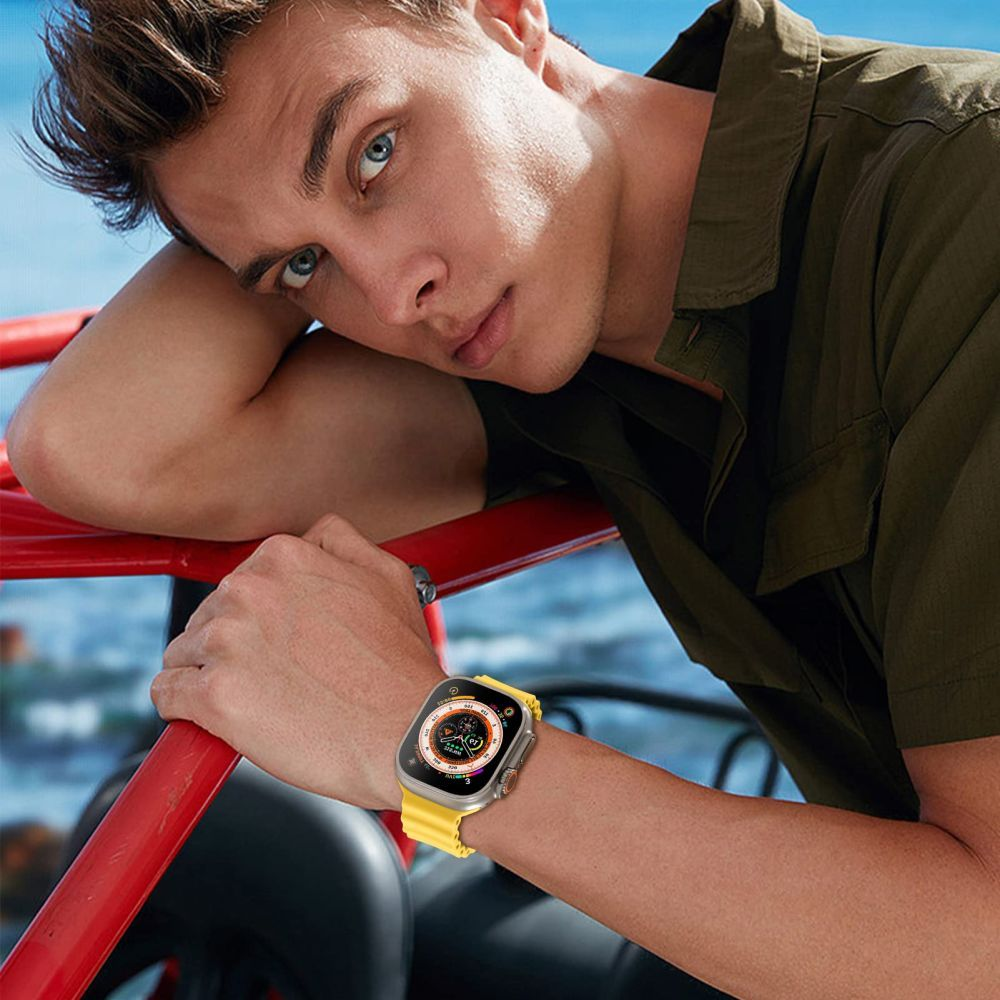 Ein Mann mit blauen Augen lehnt sich an eine rote Stange und trägt eine Smartwatch mit gelbem Armband. Er trägt ein grünes Hemd.