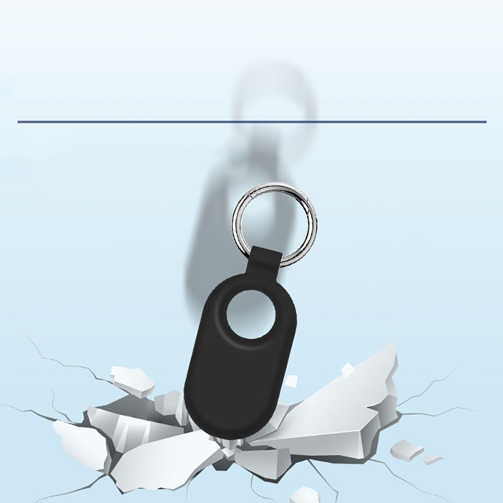 Een zwarte sleutelhanger met een zilveren ring valt naar een gebroken wit oppervlak op een lichtblauwe achtergrond.
