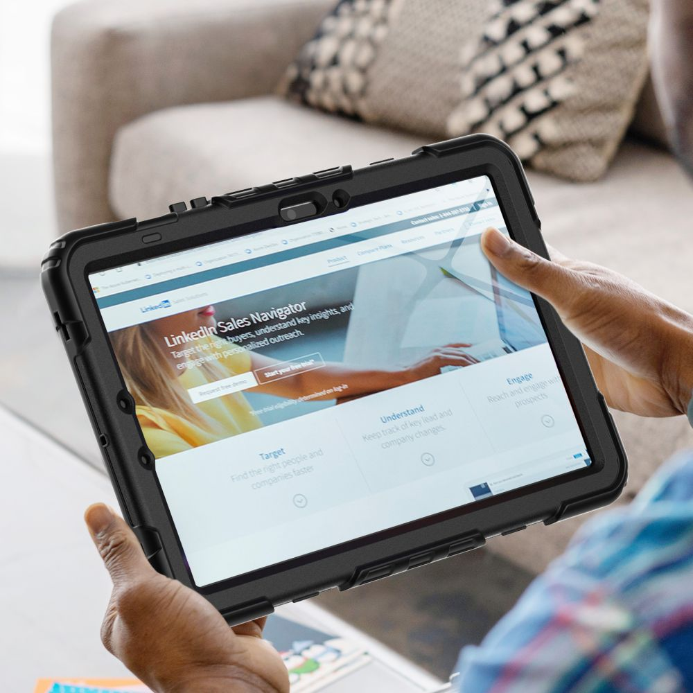 Eine Person hält ein Tablet mit einer LinkedIn Sales Navigator-Seite. Das Tablet befindet sich in einem schwarzen Gehäuse. Im Hintergrund ist eine Couch zu sehen.