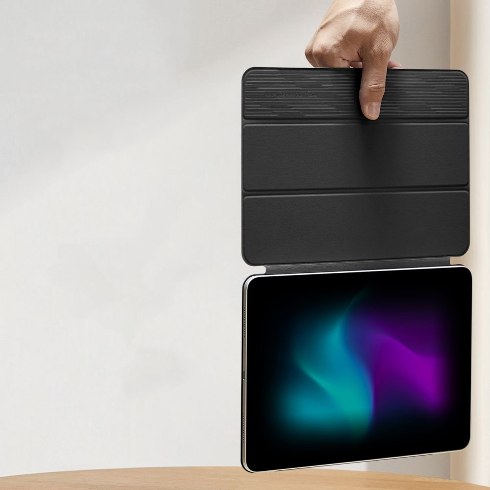 Eine Hand hält eine schwarze Tablet-Hülle. Das Tablet hat einen farbenfrohen Bildschirm. Der Hintergrund ist eine weiße Wand und ein Holztisch.