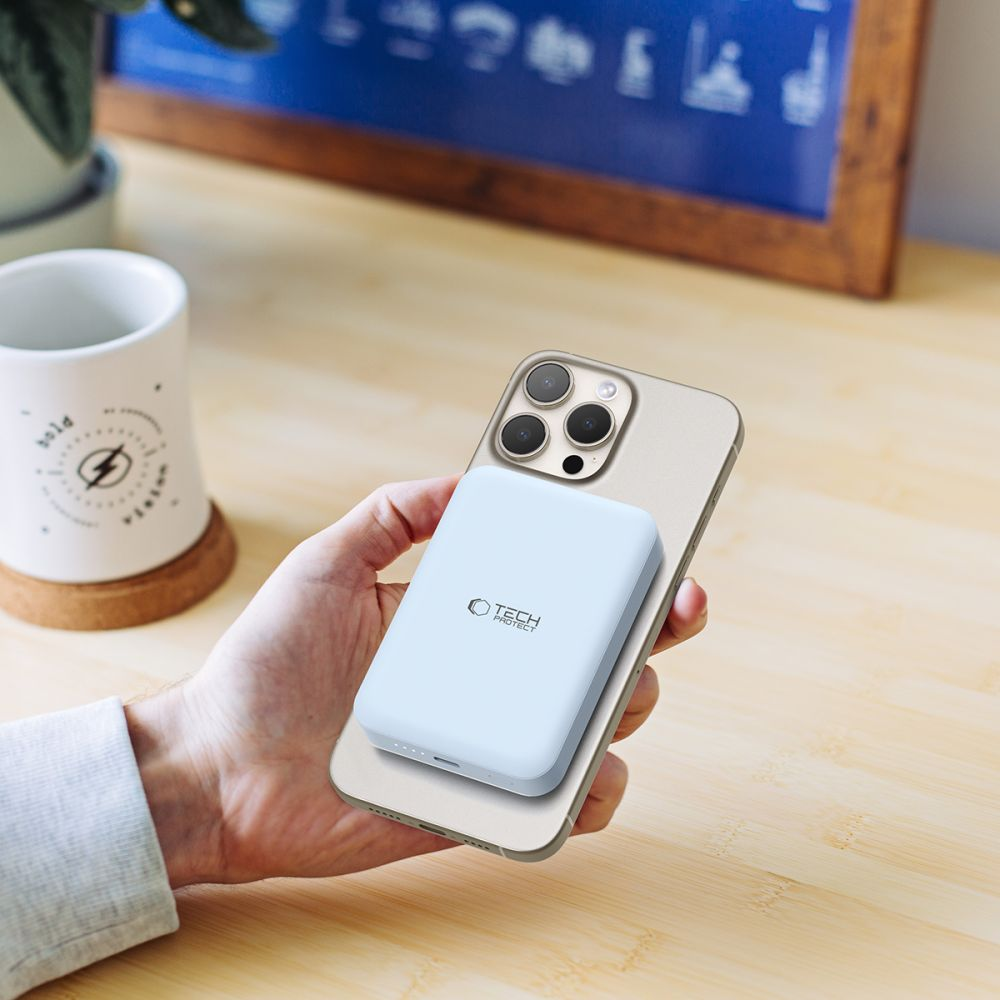 Une main tient un téléphone doré avec une batterie externe bleu clair. Le téléphone est posé sur une surface en bois.