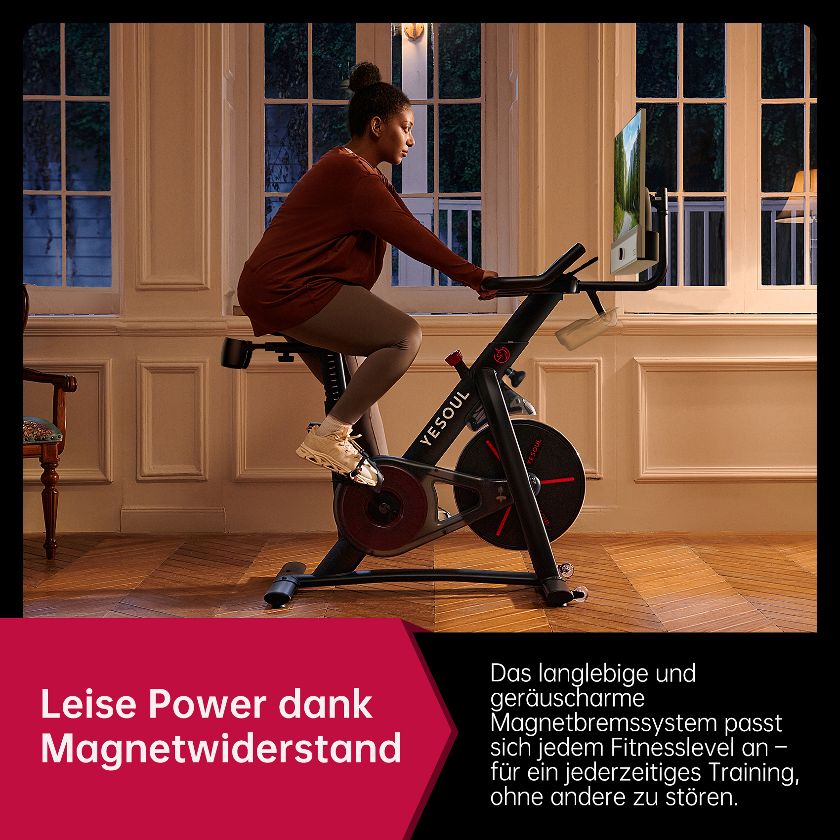 Eine Frau trainiert auf einem Heimtrainer in einem Raum mit großen Fenstern, einem Monitor und Holzböden.