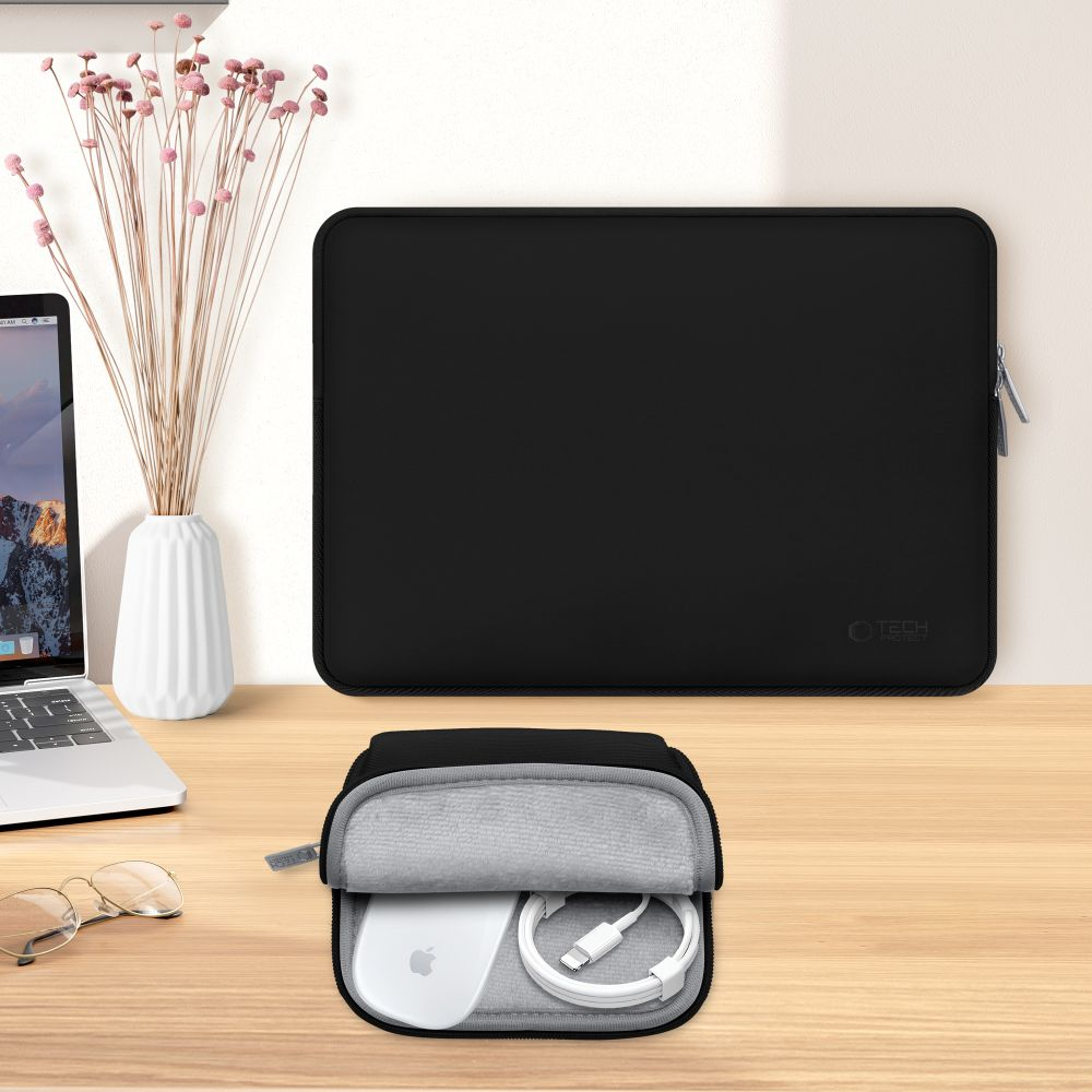Een zwarte laptoptas, hoes en accessoires op een houten tafel. Een vaas met bloemen en een laptop zijn ook aanwezig.