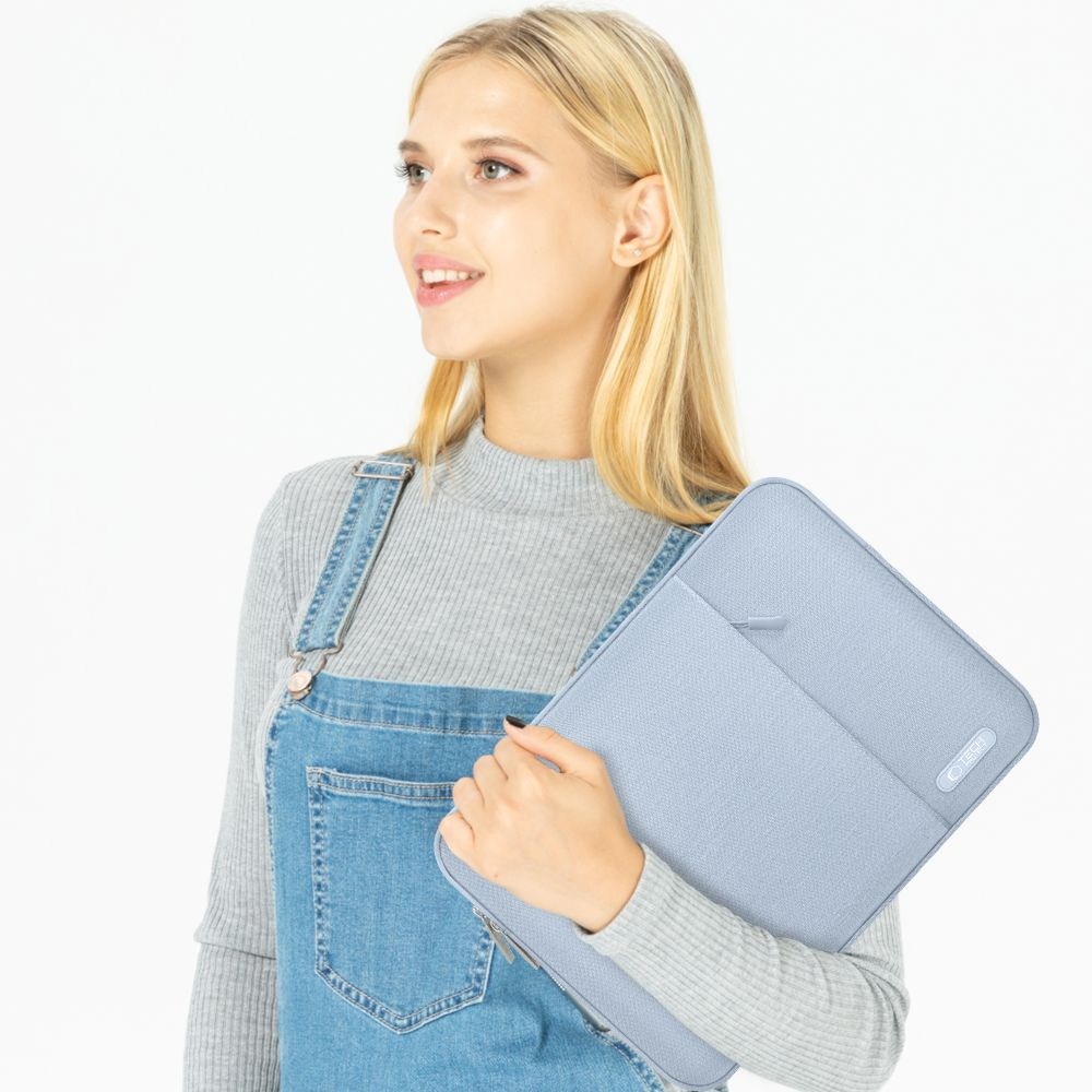 Blonde vrouw in een spijkerbroek met een lichtblauwe laptoptas. Ze glimlacht en kijkt opzij. Witte achtergrond.