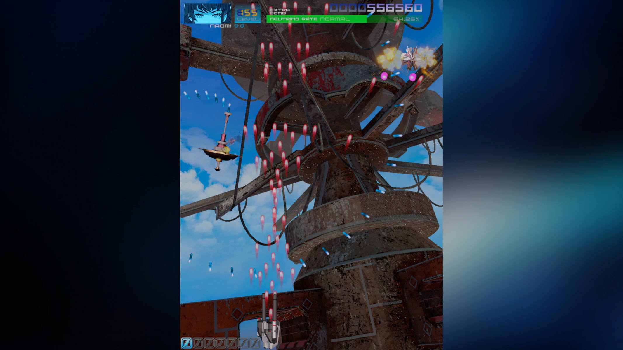 Scena di un gioco sparatutto verticale. Una grande struttura arrugginita domina il cielo. Proiettili rossi e blu riempiono lo schermo.