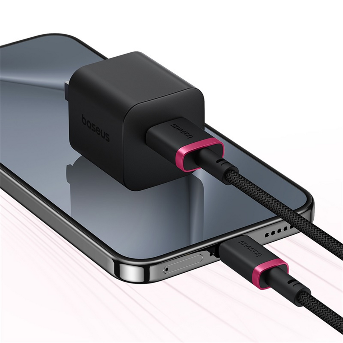 Un cargador de teléfono negro con un acento rosa está conectado a un teléfono negro. El cargador está encima del teléfono.