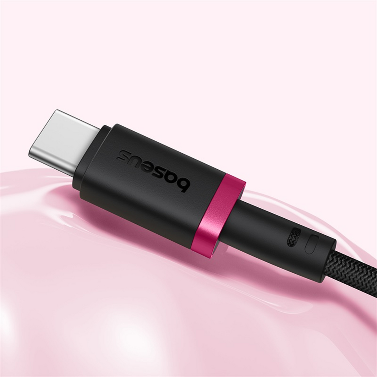 Primer plano de un cable USB-C negro Baseus con un acento rosa. El fondo es rosa suave con reflejos suaves y brillantes.