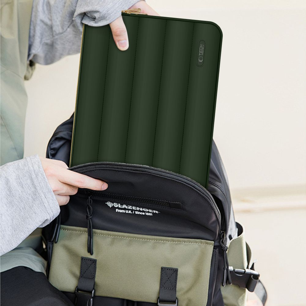 Eine Person legt eine dunkelgrüne Laptoptasche in einen schwarz-grünen Rucksack. Die Tasche hat einen goldenen Reißverschluss.