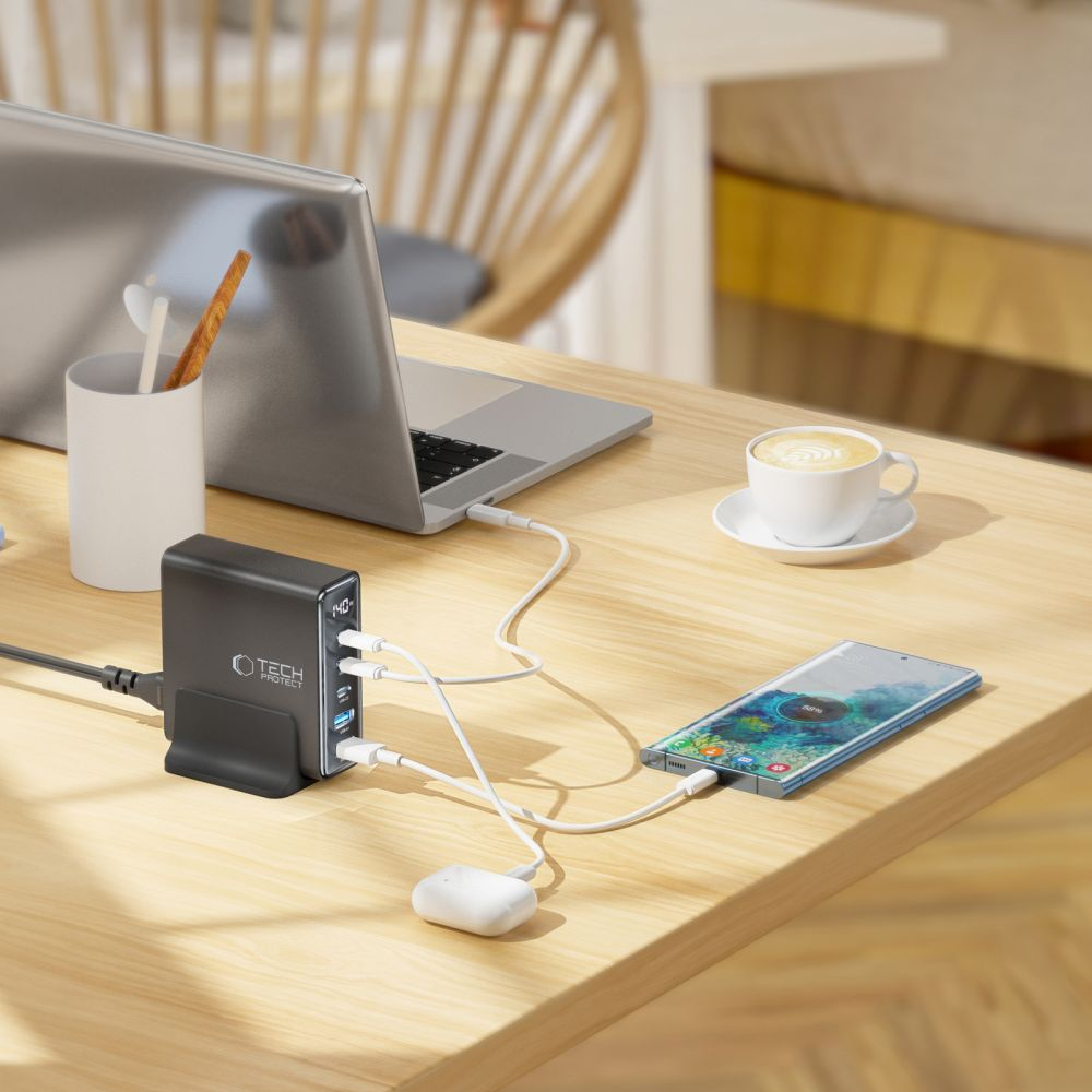 Un bureau avec un ordinateur portable, un chargeur, un téléphone, une tasse de café et une station de charge. Le téléphone se charge. L'ordinateur portable est connecté.