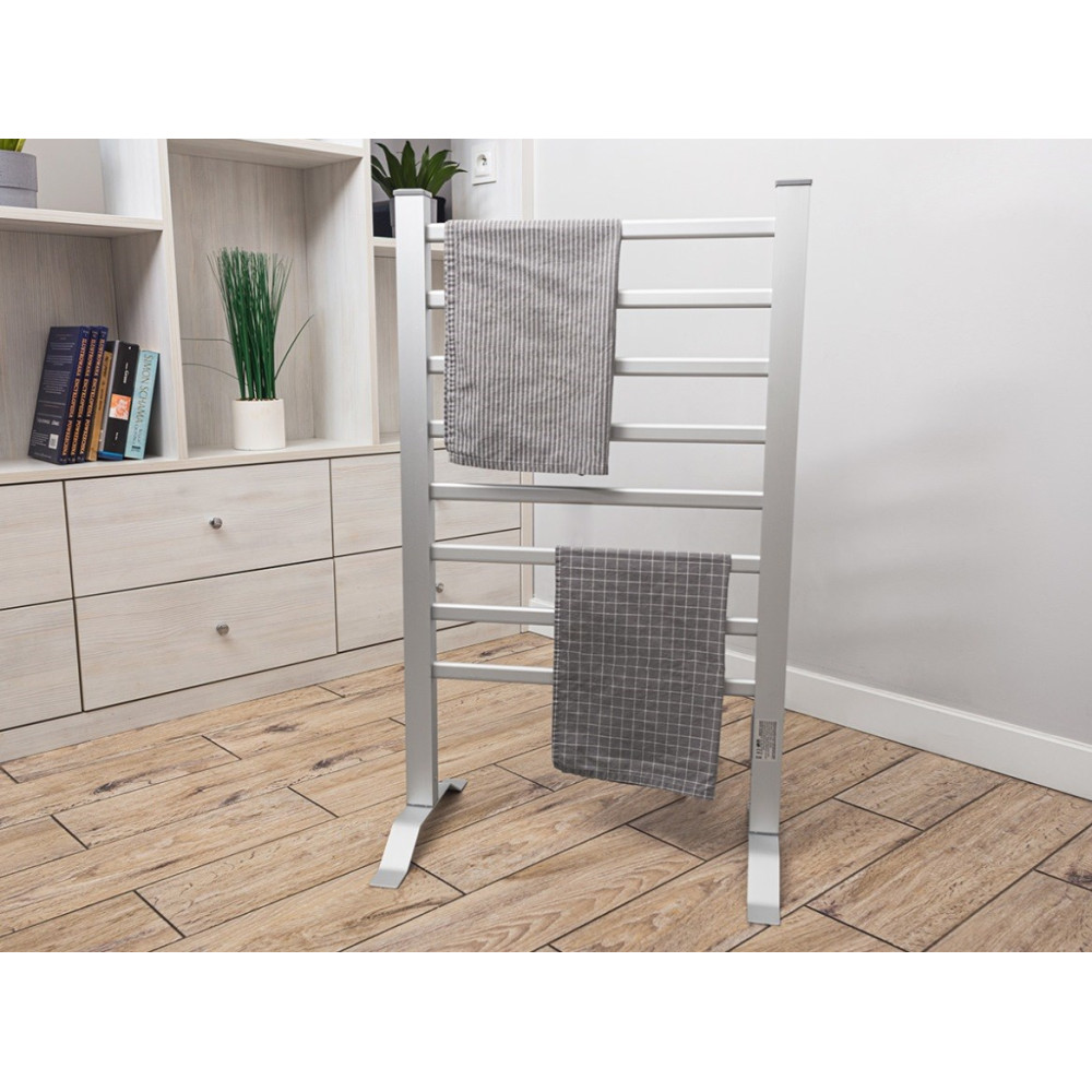 Srebrna suszarka do ręczników z dwoma ręcznikami. Tło obejmuje białą szafkę i drewnianą podłogę.