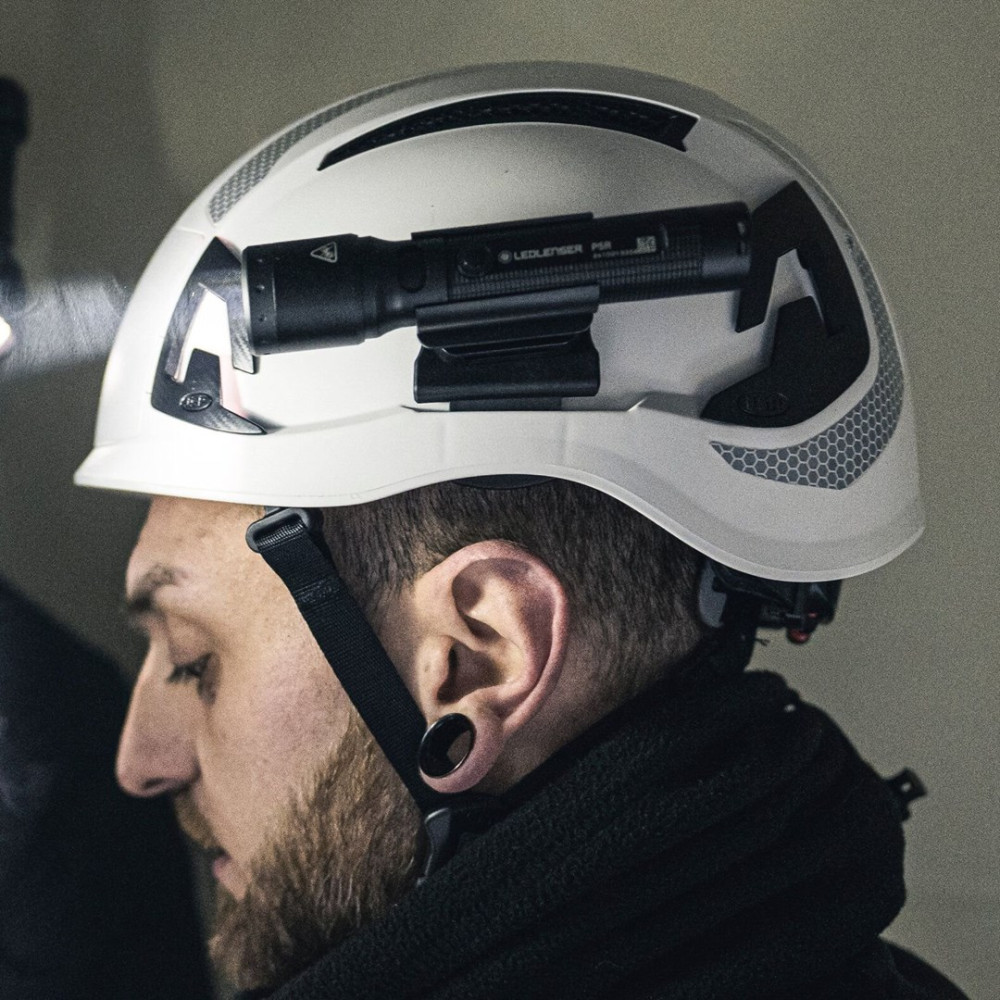 Mężczyzna w białym kasku ochronnym z czarną latarką. Ma brodę i kolczyk w uchu.