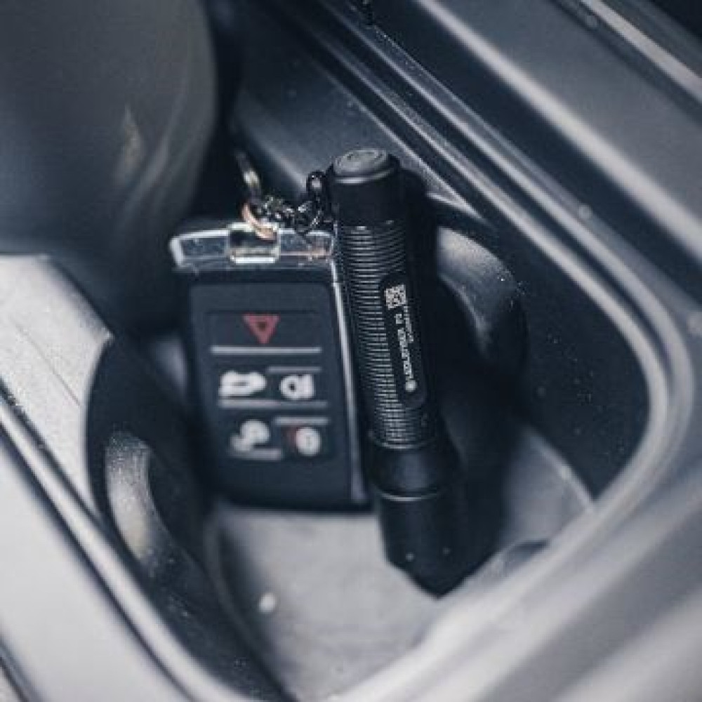 Czarna latarka i brelok do kluczy samochodowych spoczywają w schowku w samochodzie. Brelok znajduje się obok latarki.