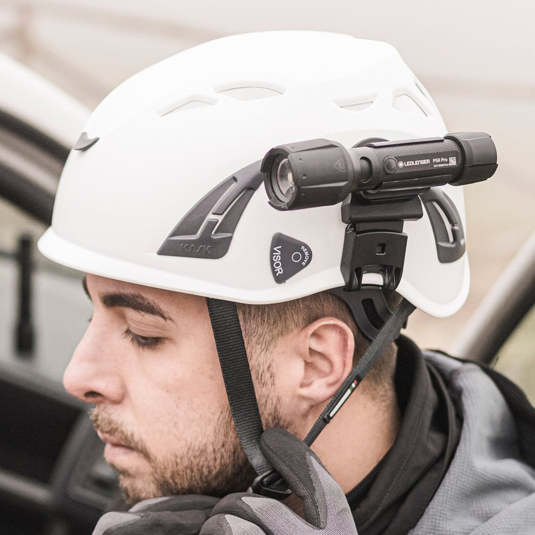 Mężczyzna w białym kasku z zamontowaną latarką LEDLENSER PSR Pro. Zapina pasek kasku. Szare rękawice.