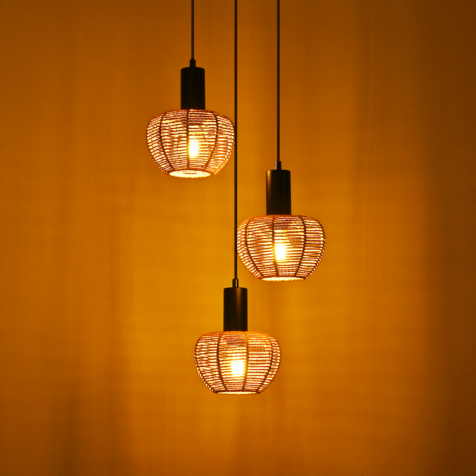 Trzy lampy wiszące z tkanymi kloszami wiszą na żółtym tle, każda z zapaloną żarówką.