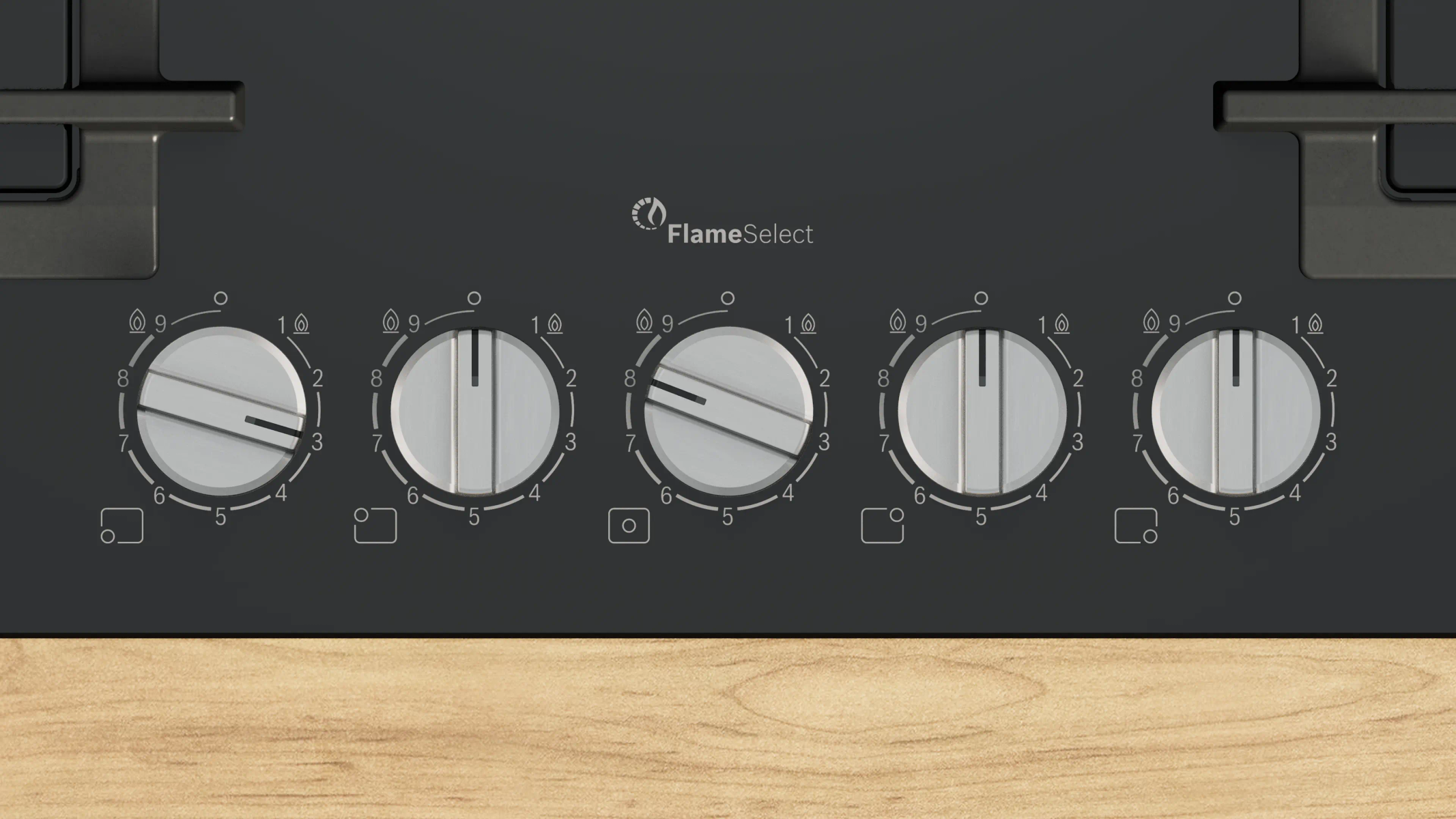 Zbliżenie czarnej płyty grzejnej z pięcioma srebrnymi pokrętłami. Każde pokrętło ma cyfry i ikonę płomienia. Tło to drewno.