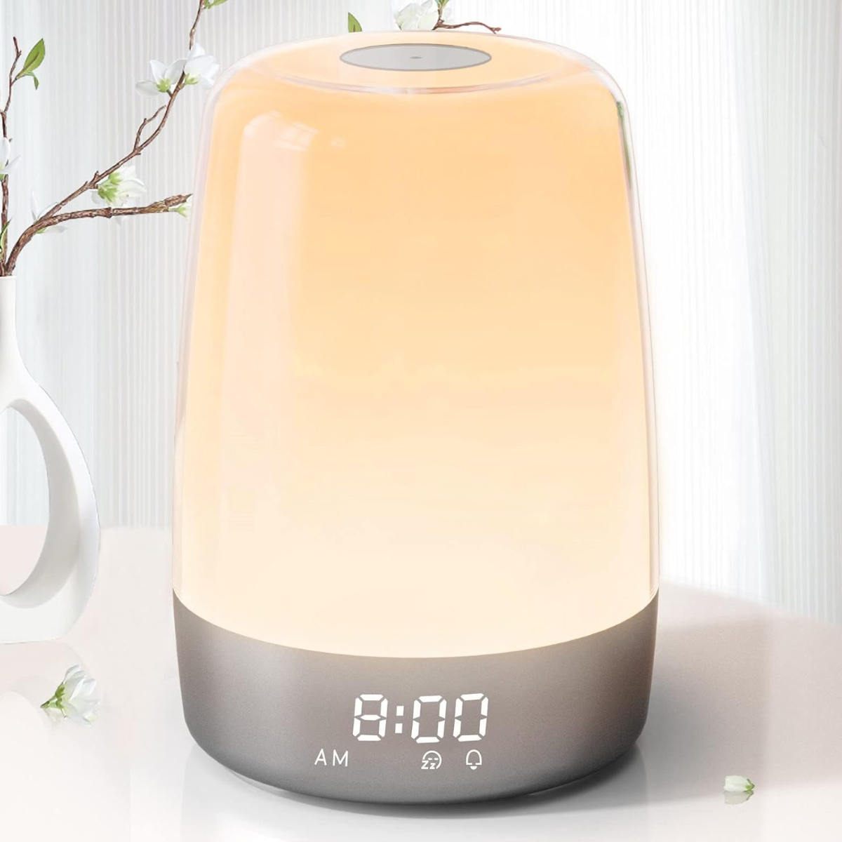 Eine leuchtende Nachttischlampe mit der Anzeige 8:00 Uhr morgens. Links eine Vase mit Blumen. Der Hintergrund ist ein weißer Vorhang.