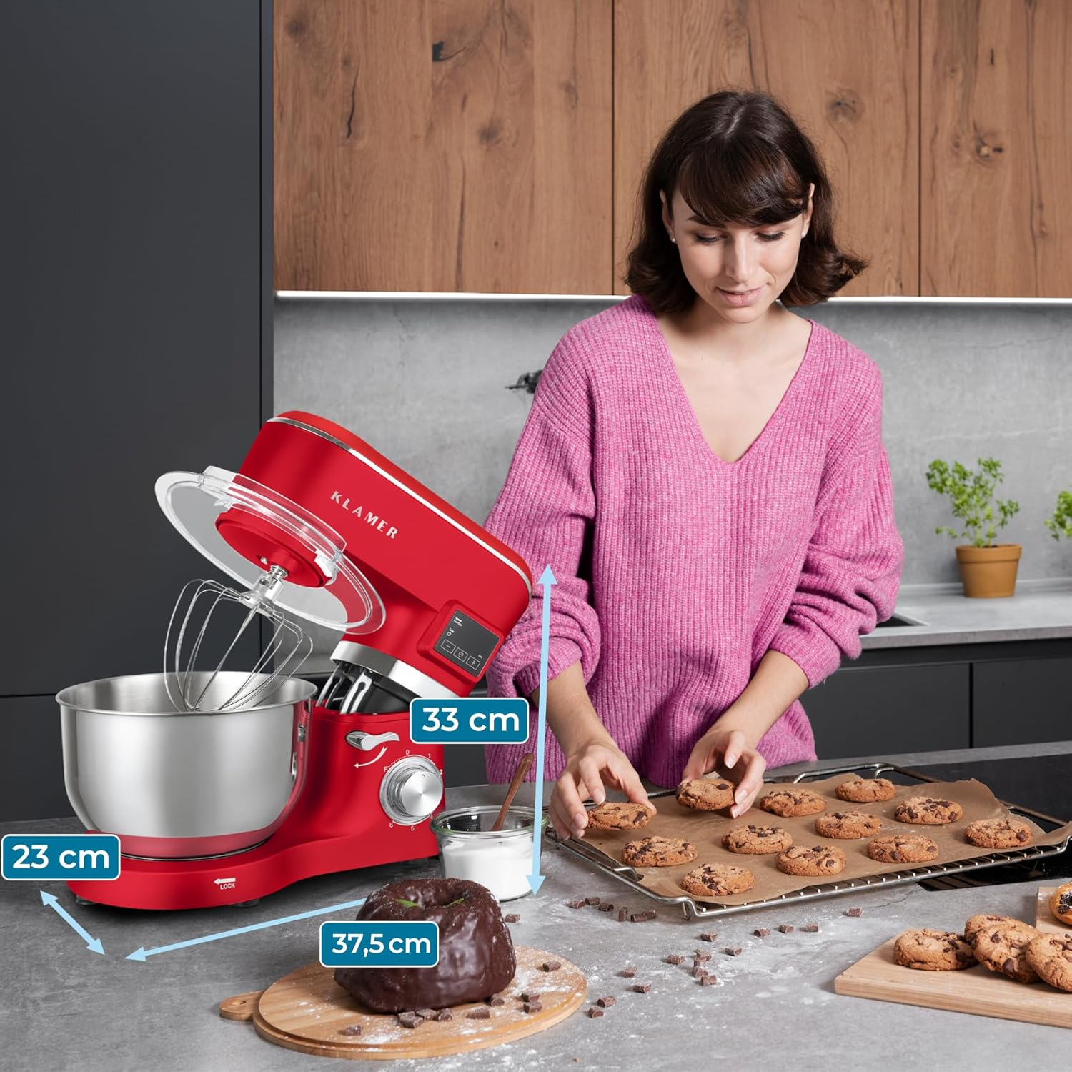 Eine Frau platziert Kekse auf einem Backblech. Im Hintergrund befindet sich ein roter Mixer. Auf einem Holzbrett liegt ein Schokoladenkuchen.