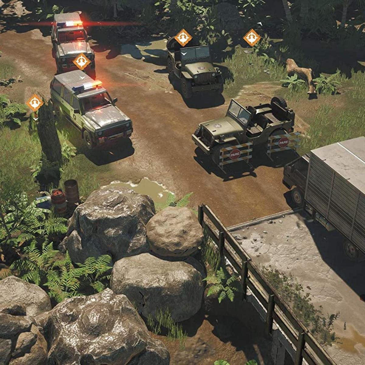 Pojazdy wojskowe na polnej drodze, otoczone zielenią i skałami. Niektóre pojazdy mają włączone światła. Ciężarówka zaparkowana po prawej.