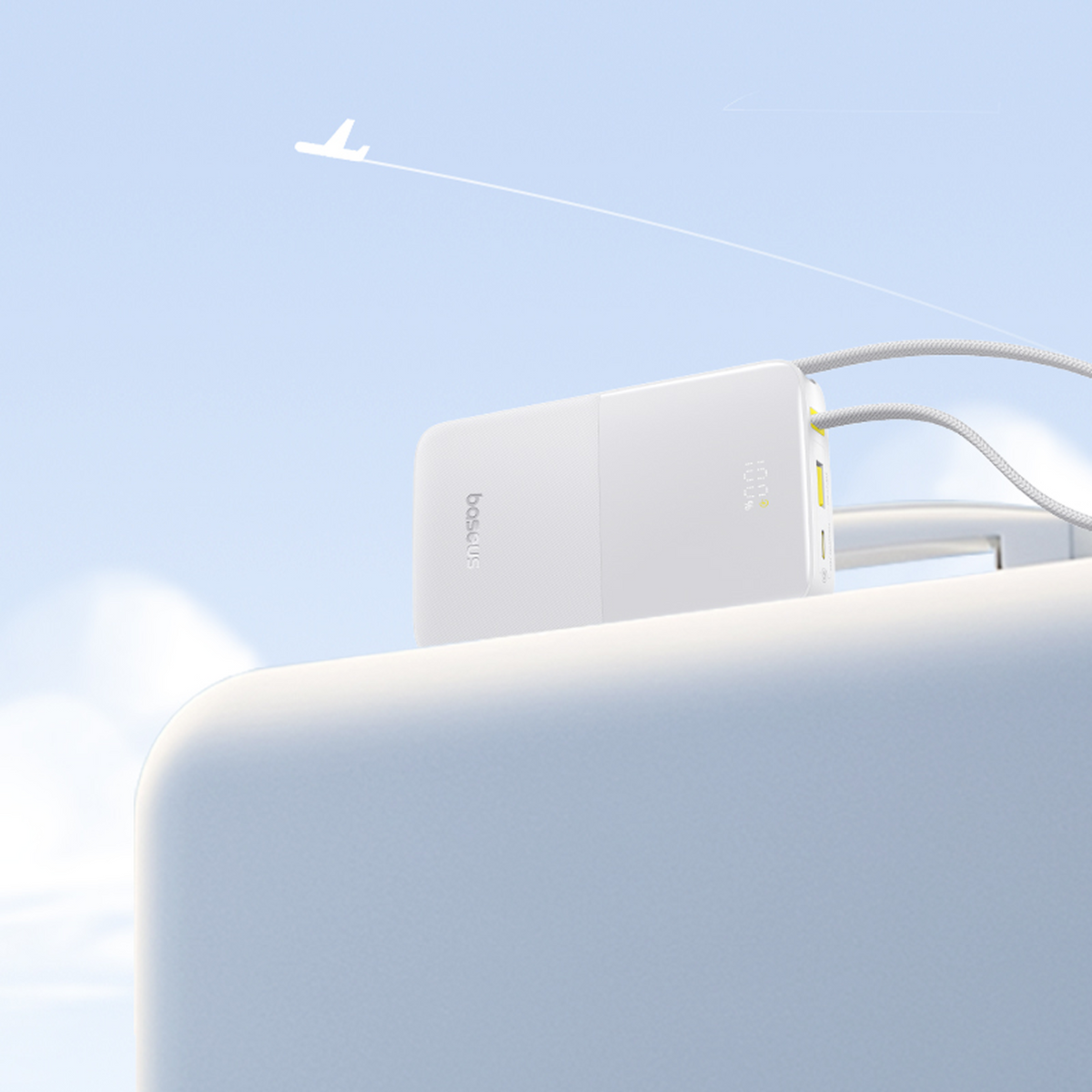 Un power bank Baseus bianco con cavi è su una superficie bianca, con una scia di aereo in un cielo blu. Il display mostra 100%.