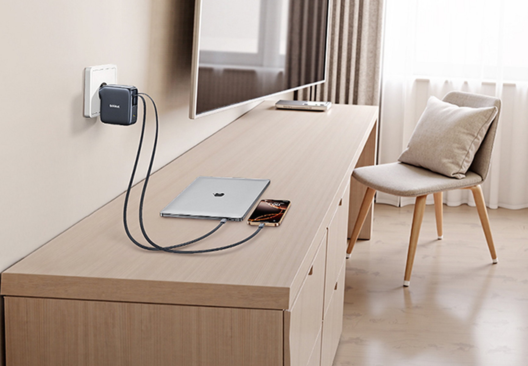 Un laptop e un telefono si caricano su un tavolo di legno. Un caricabatterie è collegato alla parete. Una sedia e una TV sono sullo sfondo.