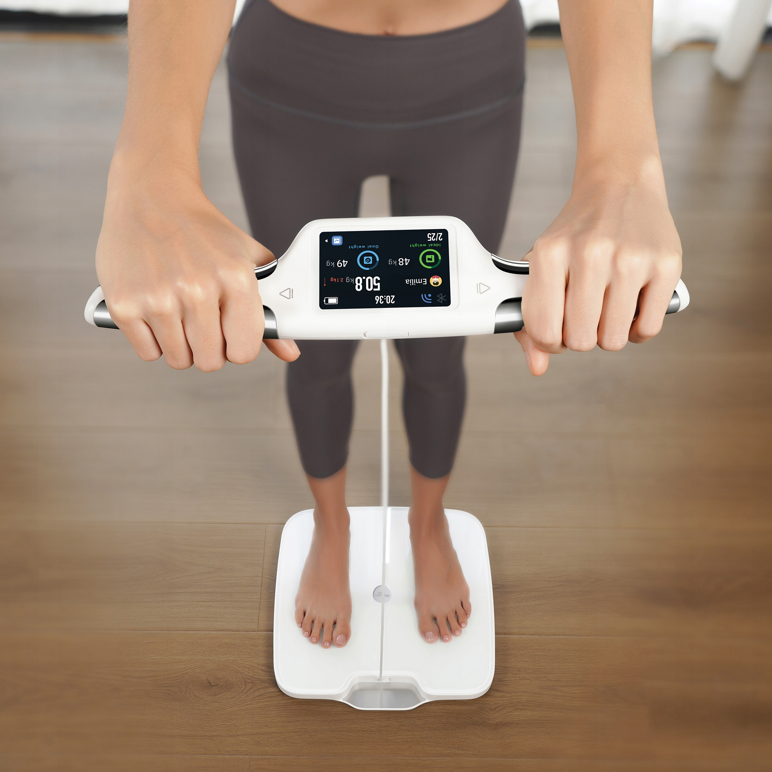 Osoba stoi na wadze cyfrowej, trzymając urządzenie. Waga pokazuje wagę i dane dotyczące zdrowia.