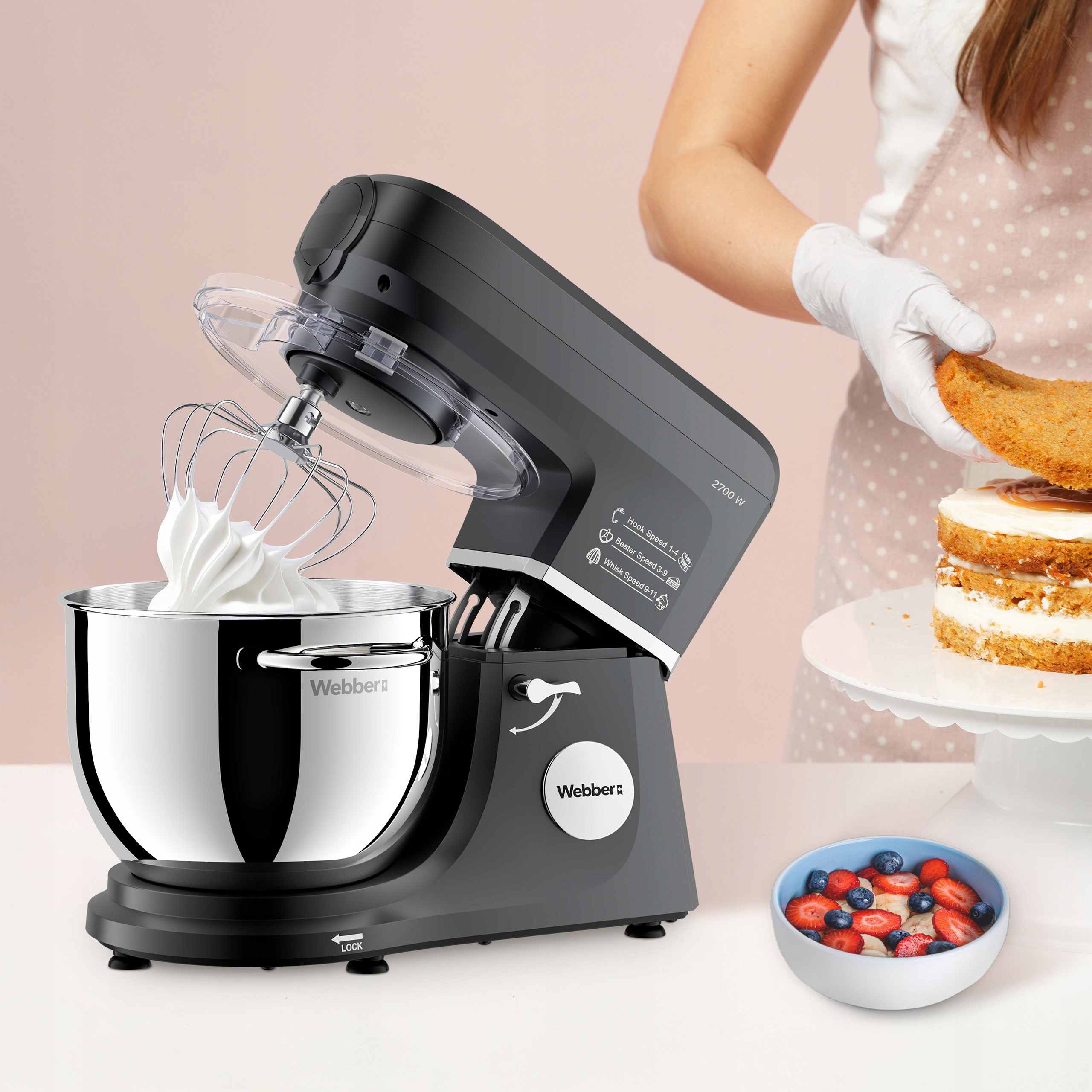 Mikser stojący z bitą śmietaną. Osoba dodaje warstwę ciasta do ciasta. Miska jagód. Różowe i białe tło.
