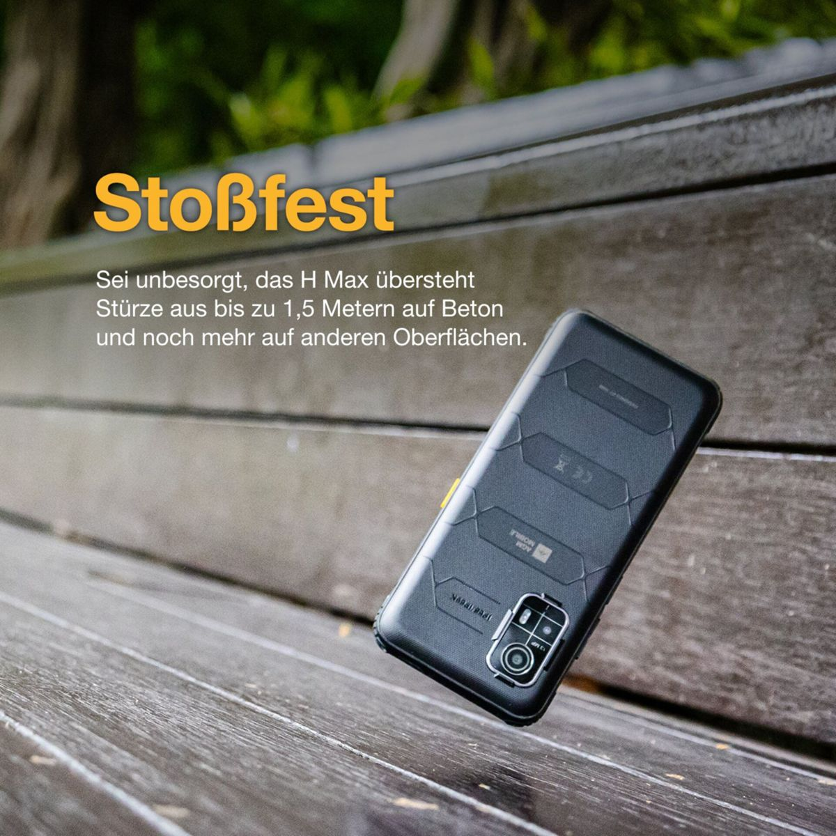 Uno smartphone nero con retro strutturato poggia su una panchina di legno. La parola 'Stoßfest' è in alto. Il testo sottostante parla di resistenza alle cadute.