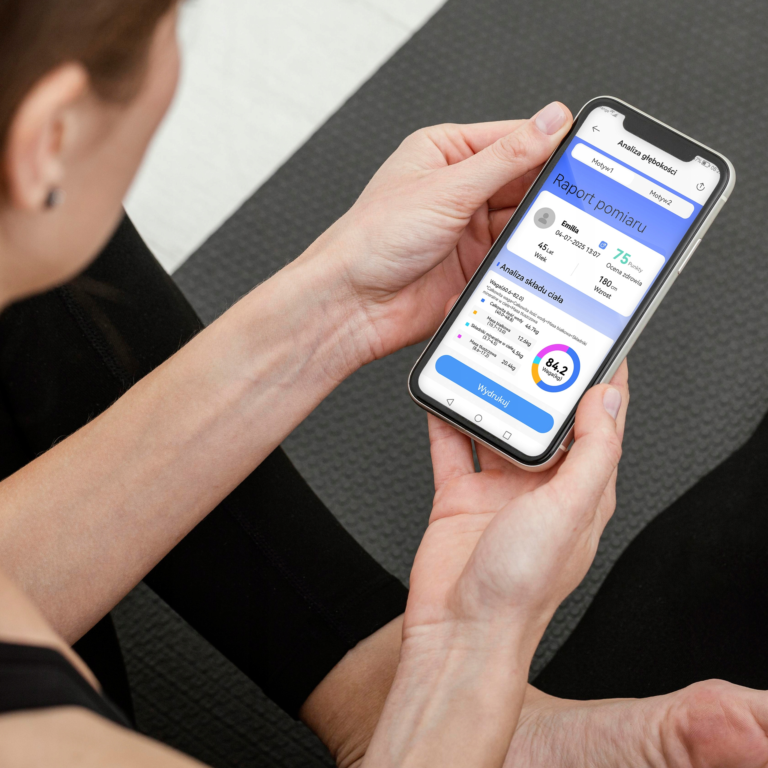 Osoba trzyma telefon z danymi zdrowotnymi. Twarz osoby jest częściowo widoczna.