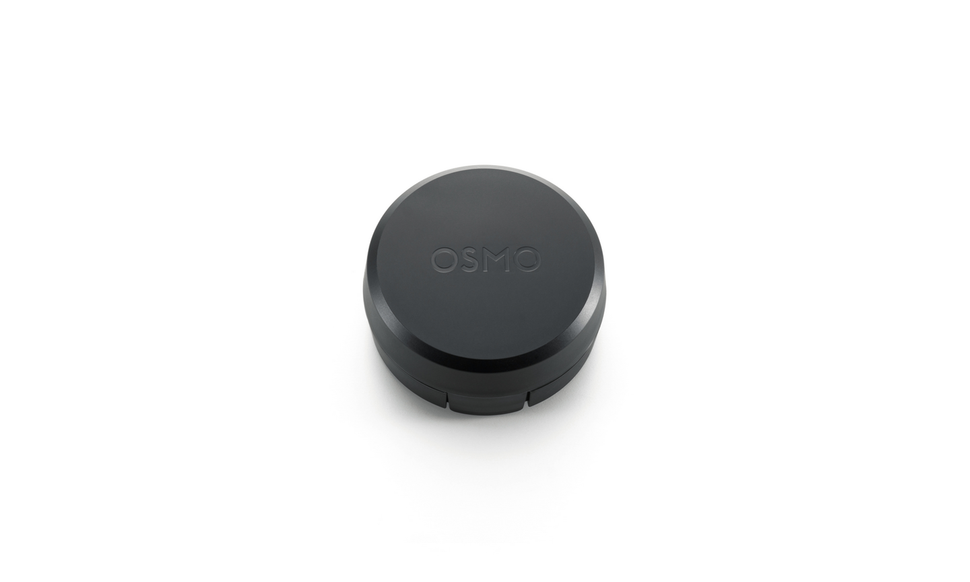 Un dispositivo Osmo negro, circular con la parte superior plana, se encuentra sobre una superficie blanca. La palabra 'OSMO' está grabada en la parte superior.
