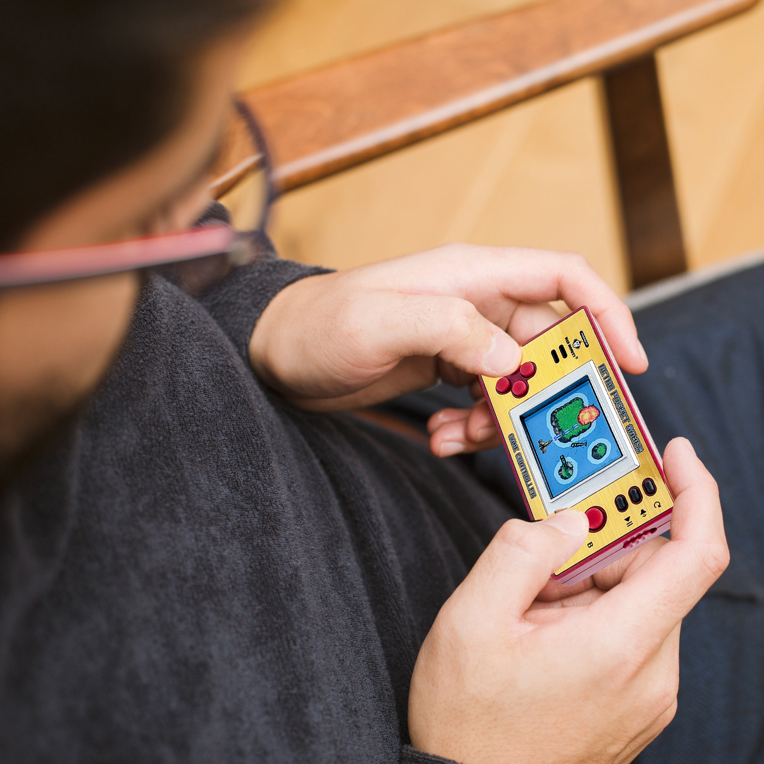 Eine Person hält eine Retro-Handheld-Spielekonsole. Die Konsole ist gelb und rot. Der Bildschirm zeigt eine verpixelte Spielszene.