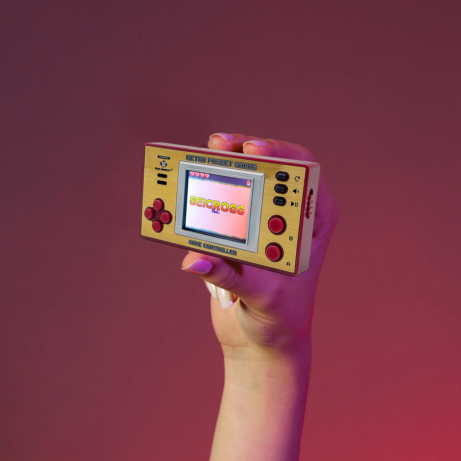 Eine Hand hält eine goldene Retro-Spielkonsole. Der Bildschirm zeigt 'SEICROSS'. Der Hintergrund ist ein Rosa-Rot-Verlauf.
