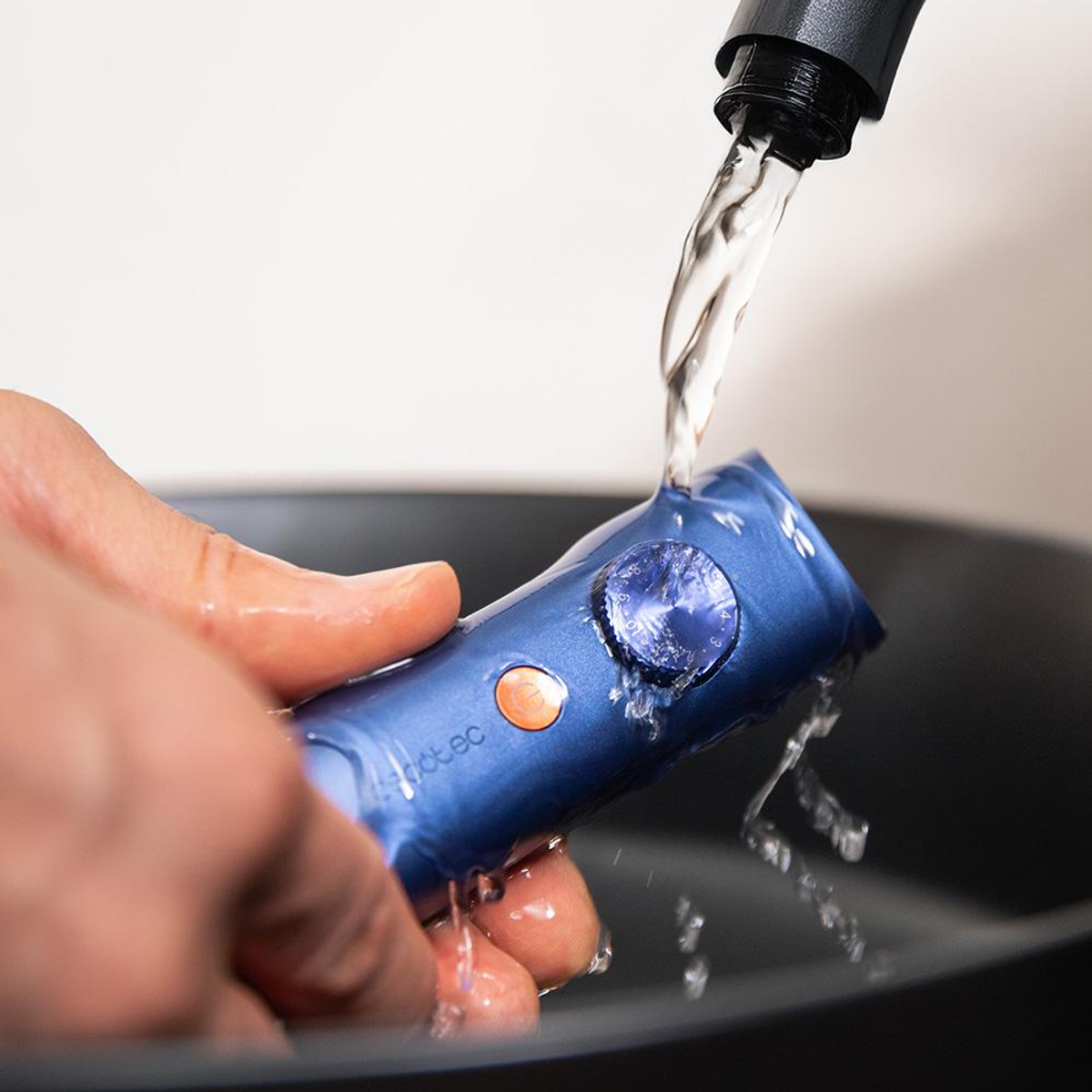 Un dispositivo blu viene risciacquato con acqua. Il dispositivo è tenuto da una mano sopra una ciotola nera. L'acqua scorre da un rubinetto nero.