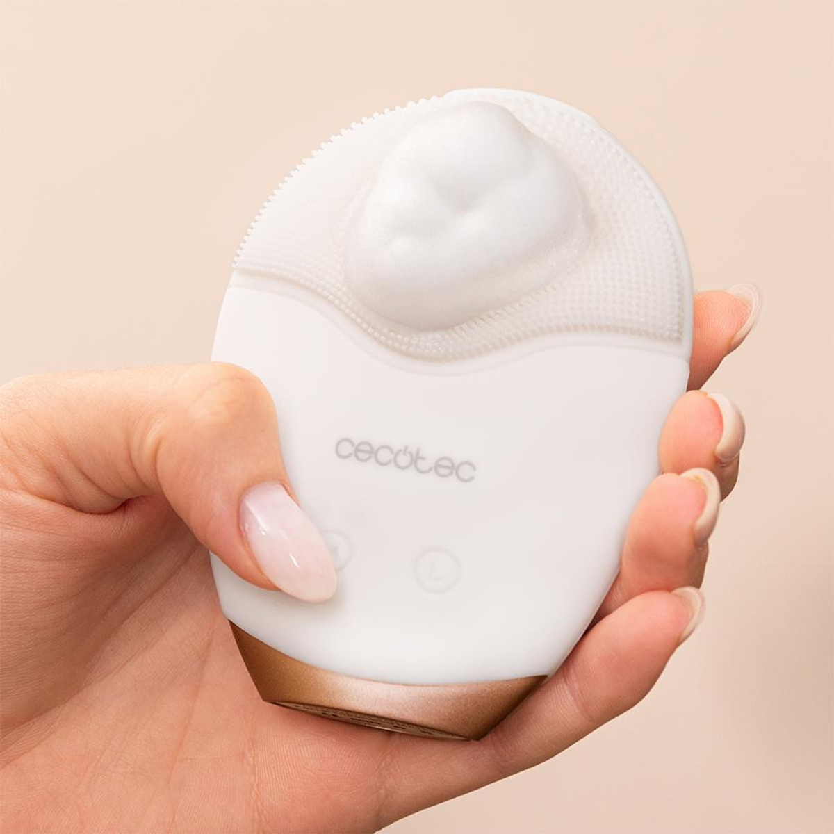 Una mano che tiene un detergente per il viso bianco con schiuma sopra. Il detergente ha dettagli oro e bianchi, il marchio è visibile.