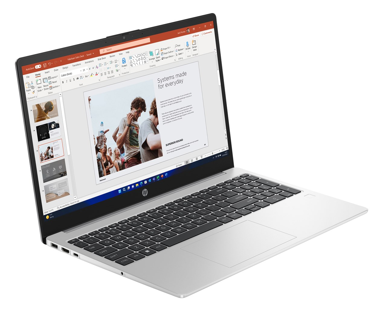 Srebrny laptop wyświetla prezentację na ekranie. Tytuł prezentacji brzmi „Systemy stworzone na co dzień”. Klawiatura jest widoczna.