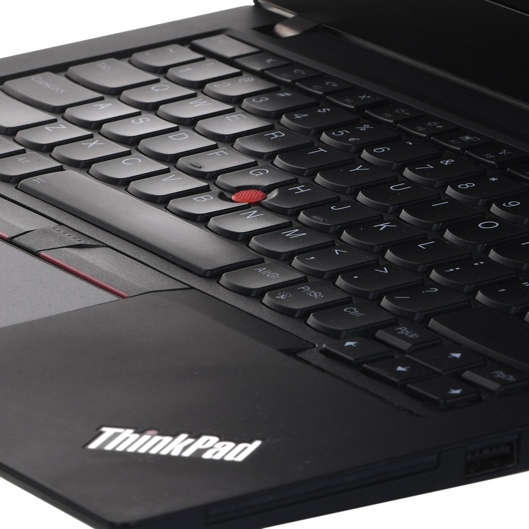 Zbliżenie laptopa ThinkPad. Czarna klawiatura z białymi literami. Czerwony trackpoint pośrodku. Widoczne logo ThinkPad.