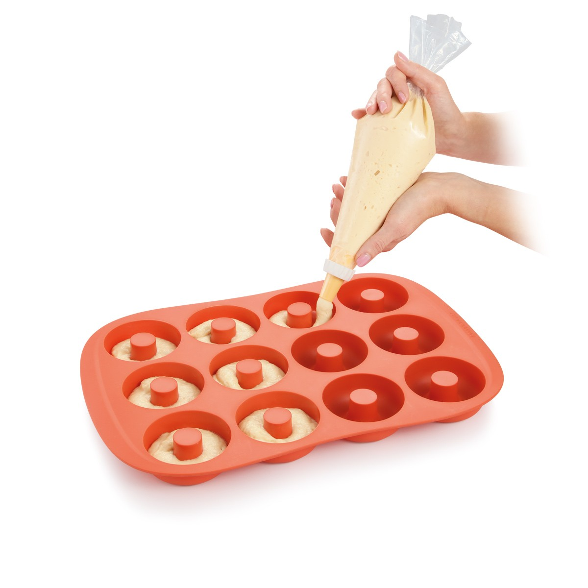 Hände drücken Teig aus einem Spritzbeutel in eine Donutform. Die Form ist orange, der Teig hellgelb.