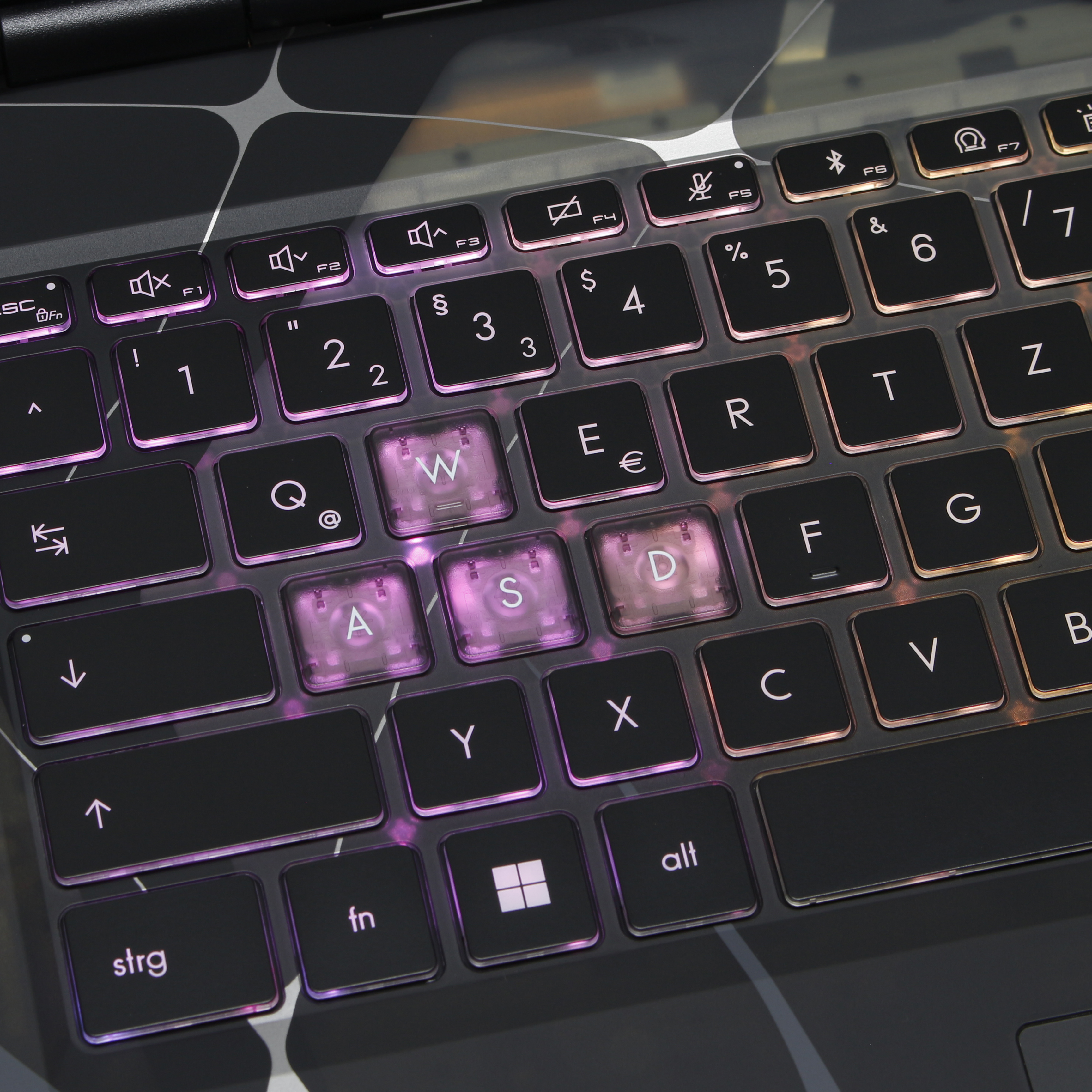 Zbliżenie klawiatury laptopa z podświetlanymi klawiszami. Klawisze W, A, S, D są podświetlone na różowo.