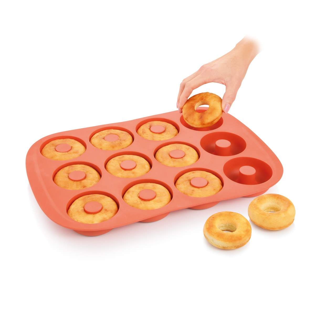 Eine Hand legt einen Donut in eine orange Backform. Gebackene Donuts sind in der Form und daneben. Weißer Hintergrund.
