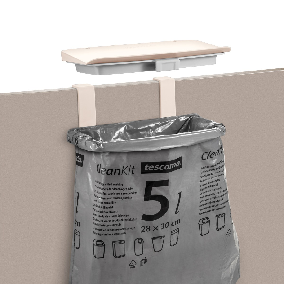 Ein grauer Müllsack hängt an einem beigen Schreibtisch. Oben ist ein weißer Deckel. Der Beutel hat Text: CleanKit und Tescoma.
