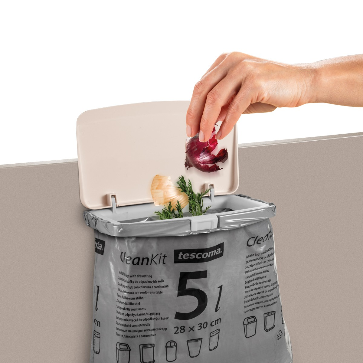 Eine Hand wirft Zwiebelschalen in einen Müllsack mit Gemüse. Der Sack ist mit 'CleanKit' und 'tescoma' beschriftet.
