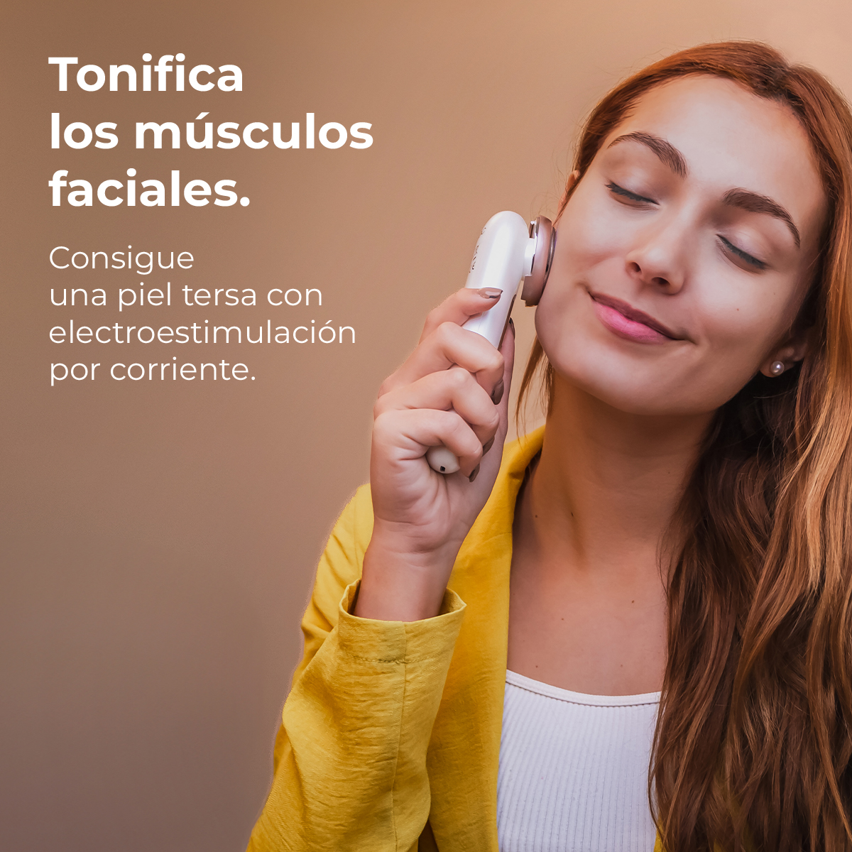 Una mujer usa un dispositivo facial en su mejilla. Viste una chaqueta amarilla y camiseta blanca, con cabello castaño y ojos cerrados.
