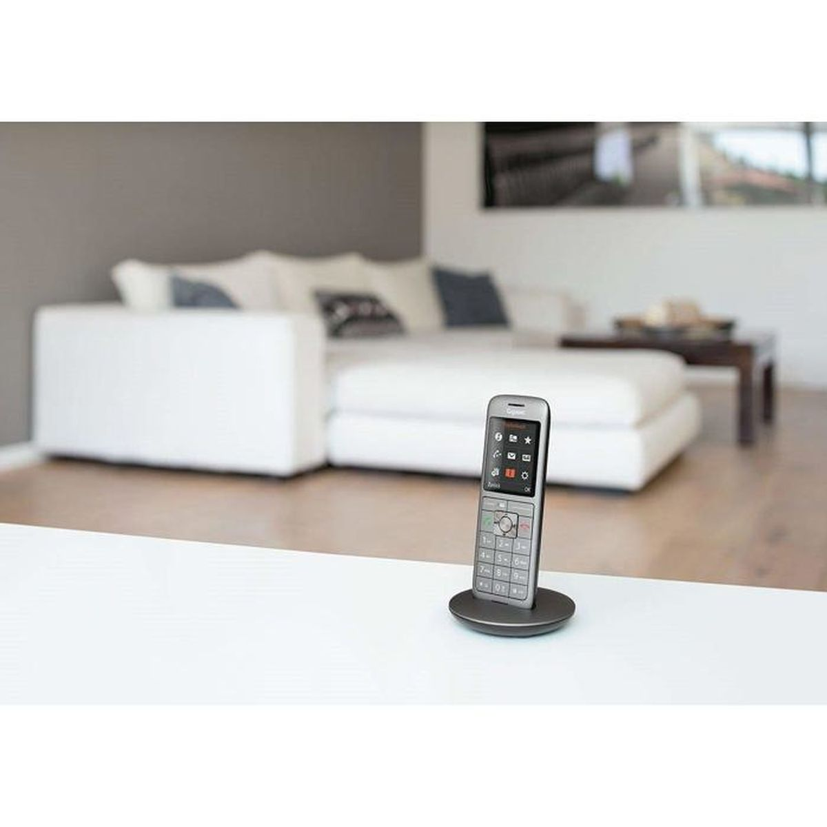 Ein silbernes schnurloses Telefon auf einem grauen Sockel auf einem weißen Tisch. Eine weiße Couch und ein Couchtisch sind verschwommen im Hintergrund.