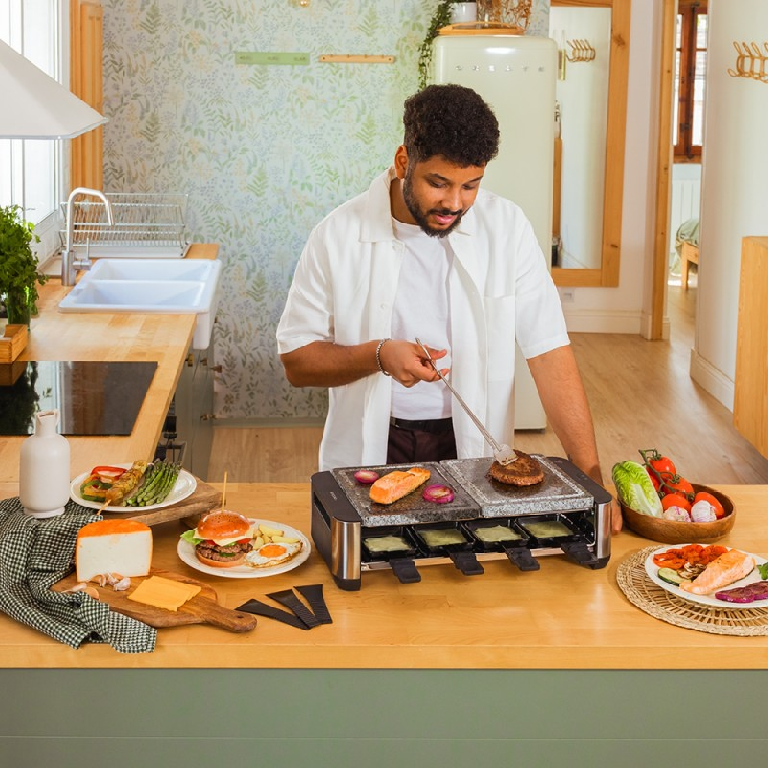 Mężczyzna grilluje jedzenie na grillu do raclette. Burgery, warzywa i łosoś na blacie.
