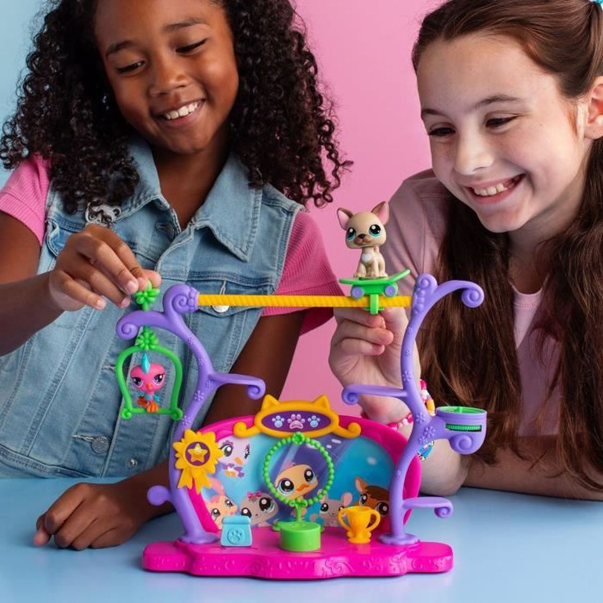 Dos niñas sonrientes juegan con un juego de juguetes rosa con figuras de animales. Un juguete de perro está en una barra amarilla y otros juguetes debajo.