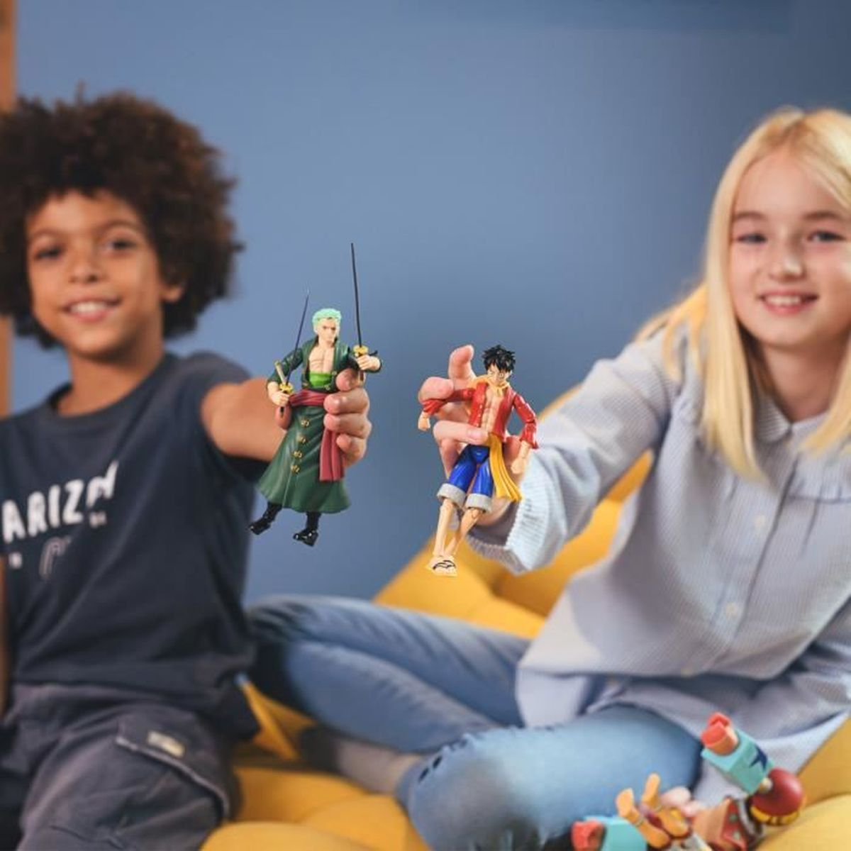 Dos niños sostienen figuras de anime. Un niño sostiene una figura vestida de verde con espadas. Una niña sostiene una figura vestida de rojo.