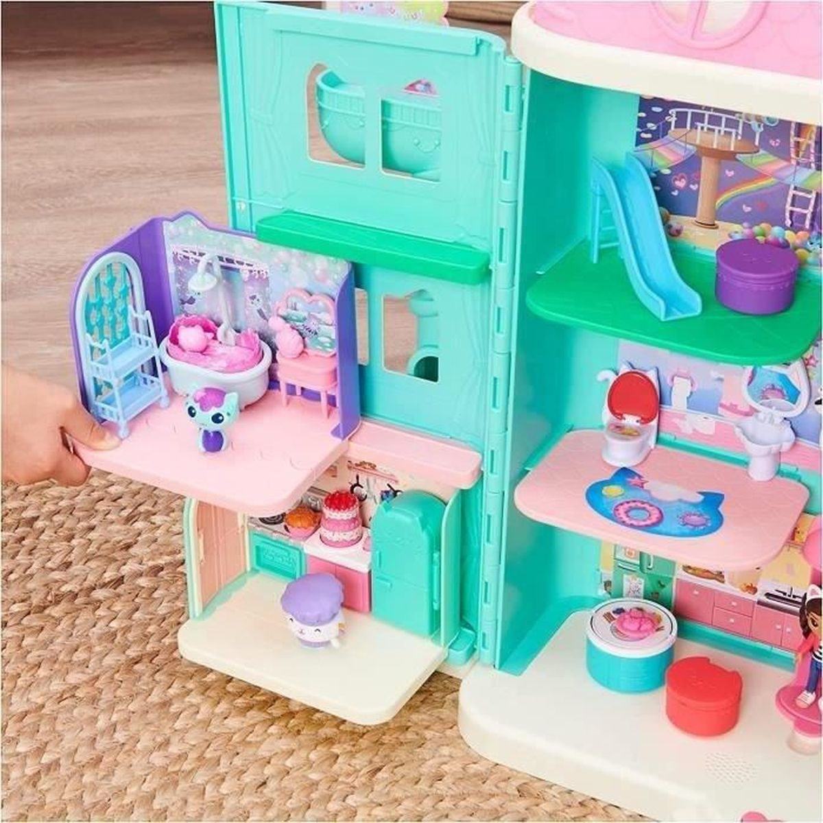 Ein buntes Puppenhaus mit mehreren Etagen. Es hat ein Badezimmer, eine Küche und einen Spielbereich mit Rutsche. Mehrere kleine Spielzeuge sind sichtbar.