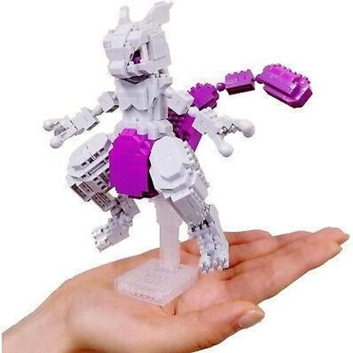 Eine Hand hält eine weiße und lila Lego-ähnliche Mewtwo-Figur. Sie steht auf einem klaren Ständer. Der Hintergrund ist unscharf.