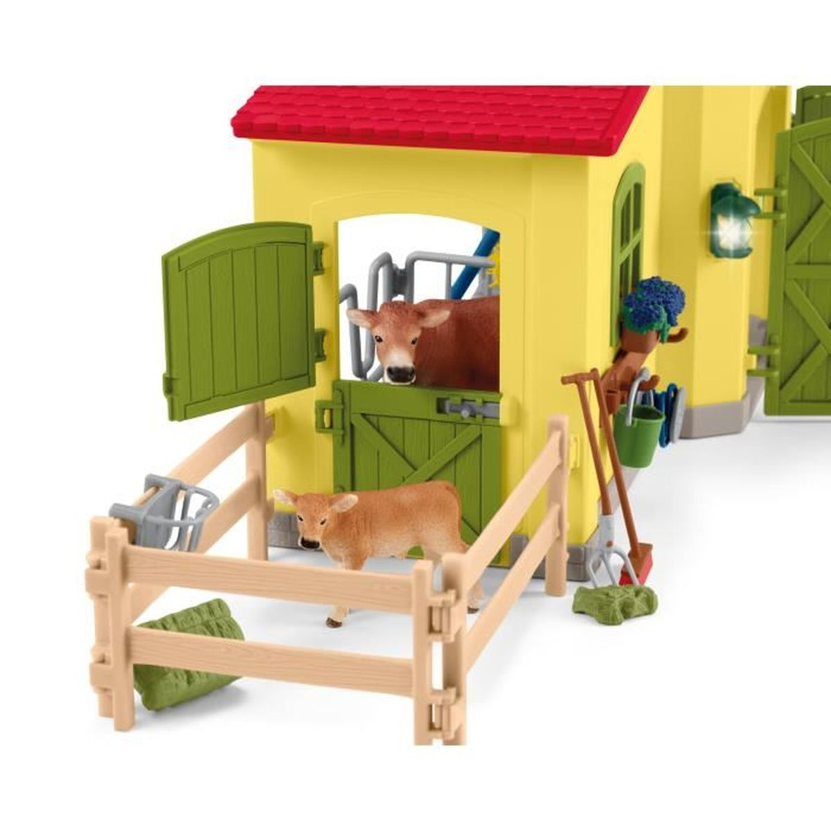 Een speelgoedboerderij met koeien, een schuur en landbouwwerktuigen. Er zijn twee koeien zichtbaar, een in een stal en een in een omheining.