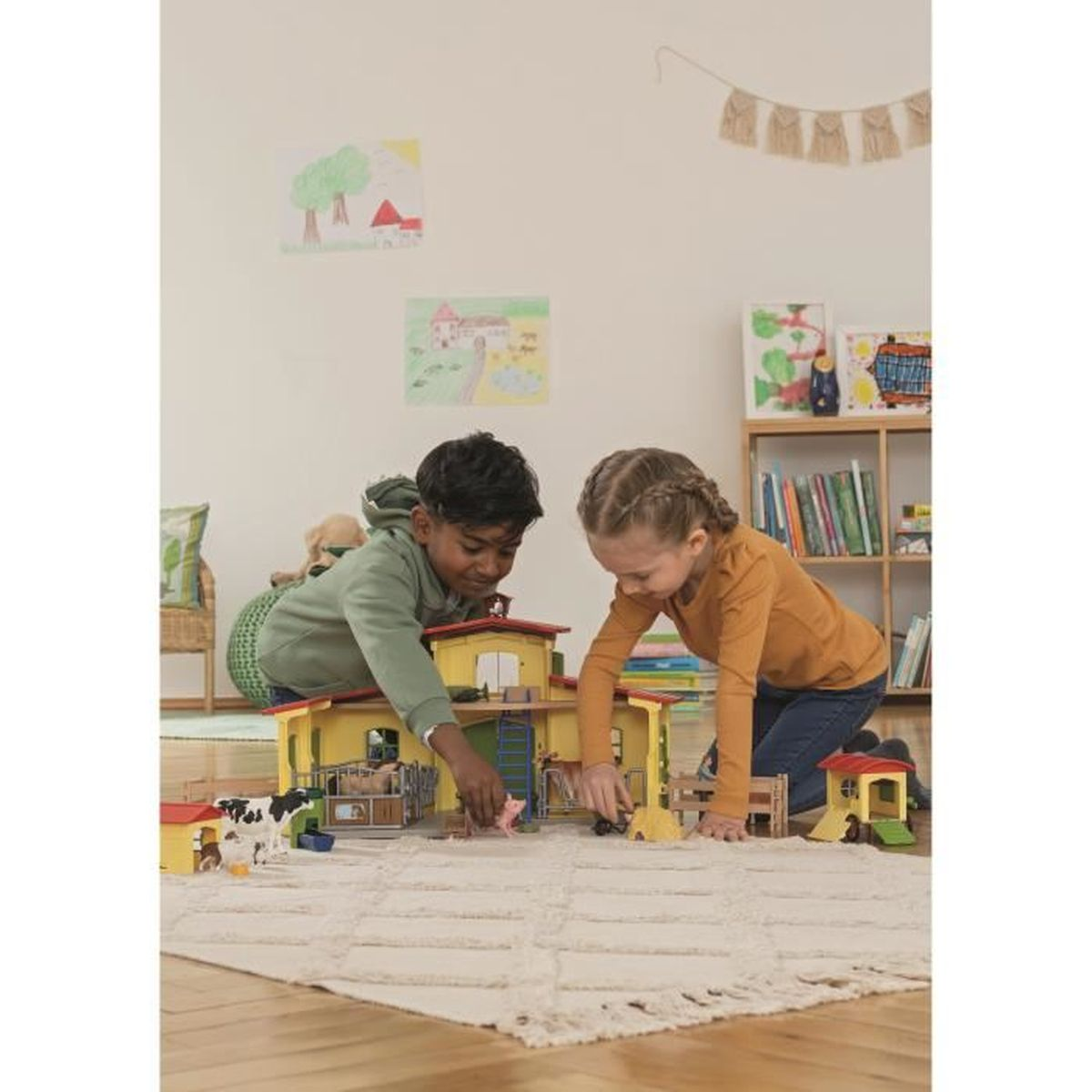 Twee kinderen spelen met een speelgoedboerderij op een kleed. De boerderij heeft een geel gebouw. Tekeningen en een boekenrek staan op de achtergrond.