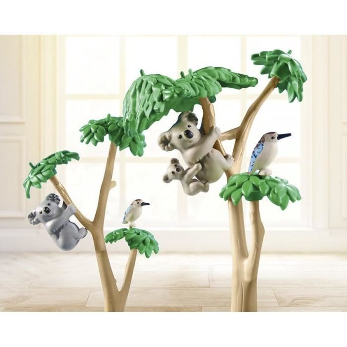 Scena giocattolo: Koala che si arrampicano sugli alberi con foglie verdi, uccelli appollaiati sui rami. Tronchi marroni chiari su sfondo chiaro.